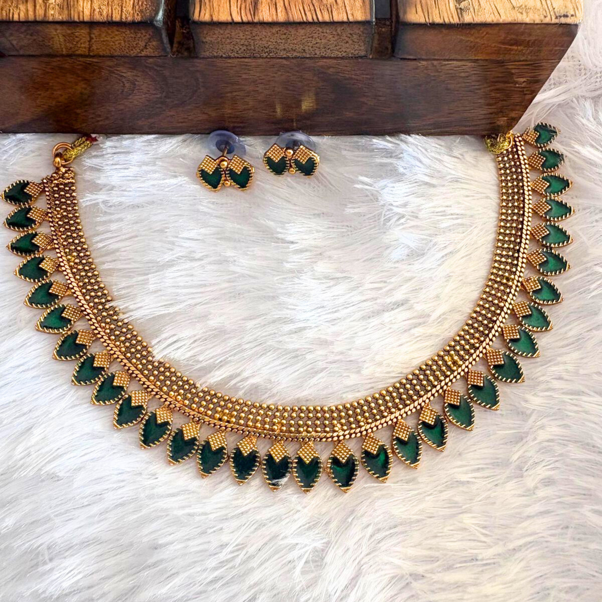 Traditional Kerala antique gold finish necklace with teardrop ruby stones and matching studs on a white fur background