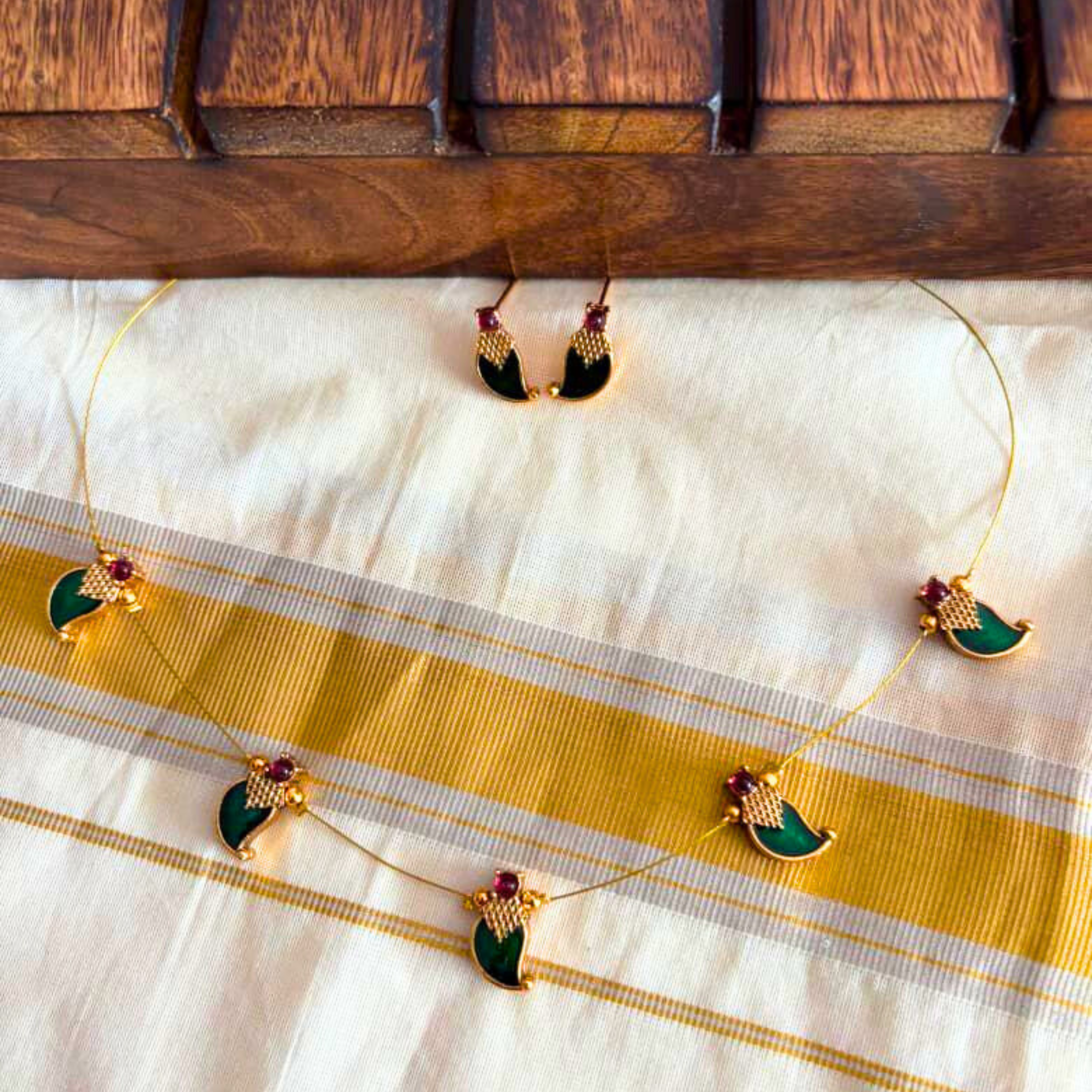 Traditional Kerala green Palakka invisible necklace with floating leaf motifs and matching studs on a Kasavu fabric background