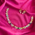 Intricate multi-color stone floral vine necklace with matching pearl-drop earrings on a rich magenta fabric background