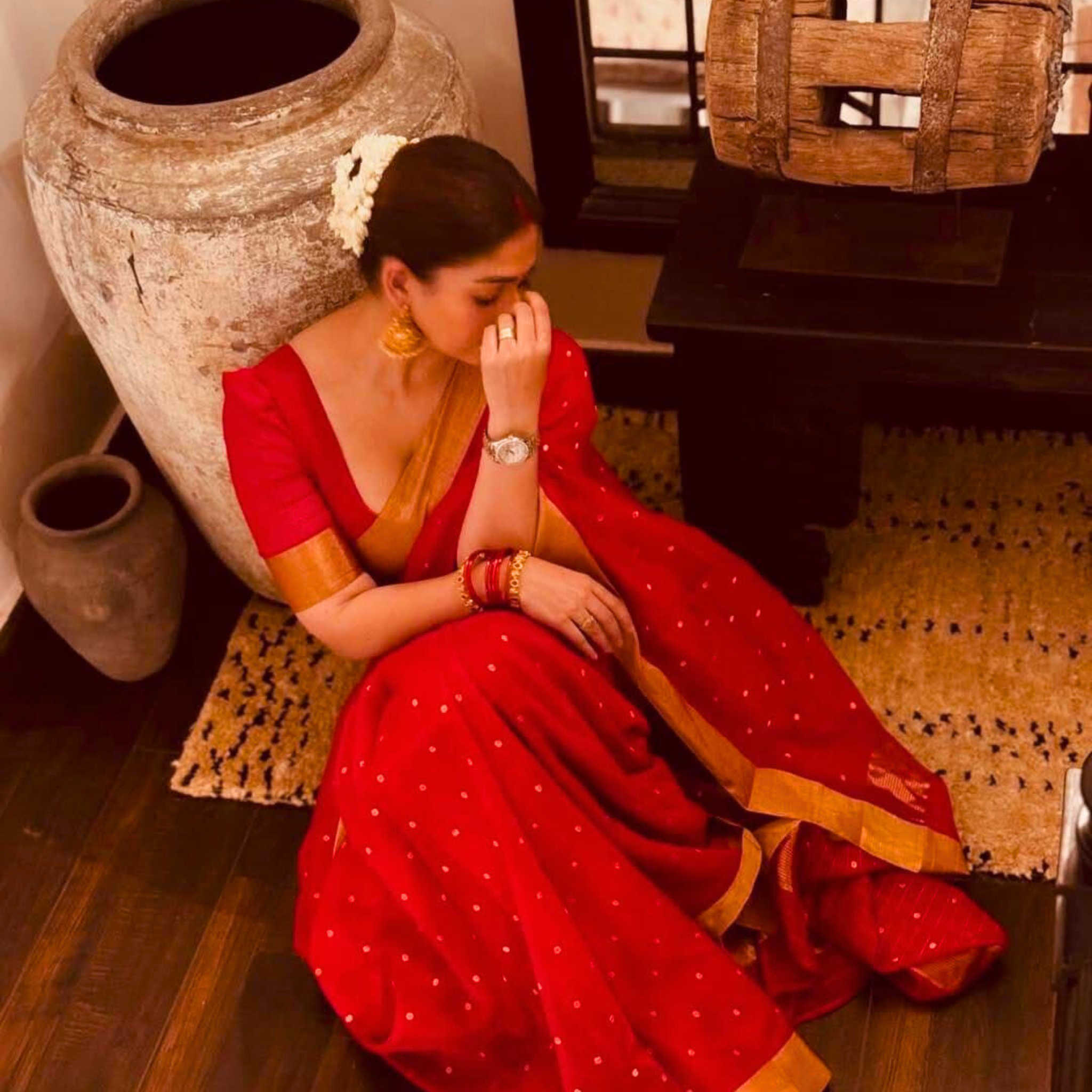 Actress Nayanthara in a traditional red and gold saree posing near a wooden elephant statue