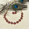 Antique matte gold finish Dayza necklace with ruby floral motifs and matching studs on a cream background with peacock feathers